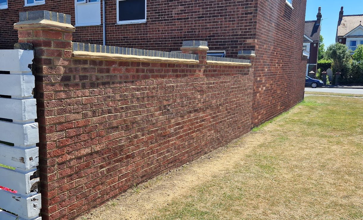 Long red-brick front boundary wall with piers and a coping finish
