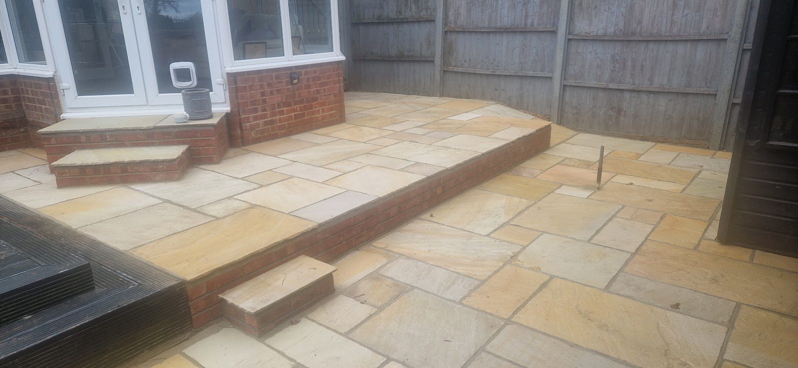 Raised sandstone patio with a brick retaining edge and steps